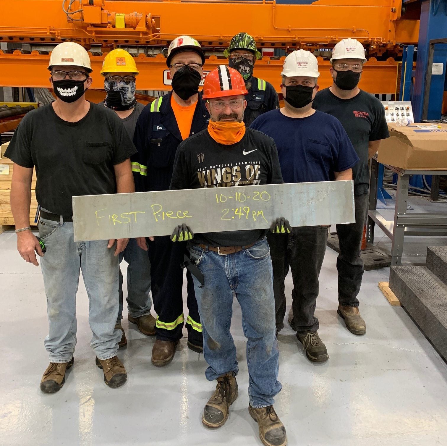 Man holding up steel saying "first piece 10-10-20, 2:49 PM" with group of guys behind him